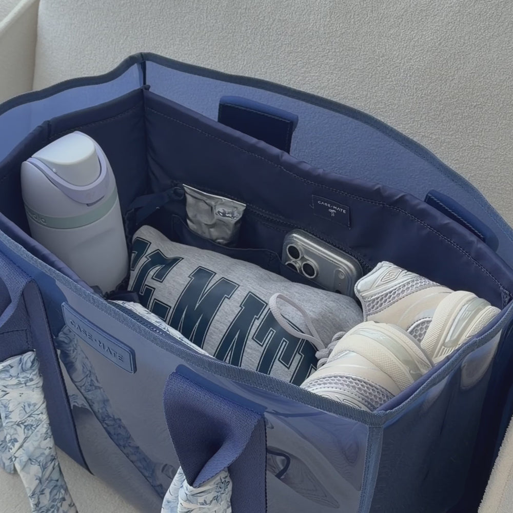 Woman packing tote bag with various items while the bag sits on a cream accent chair