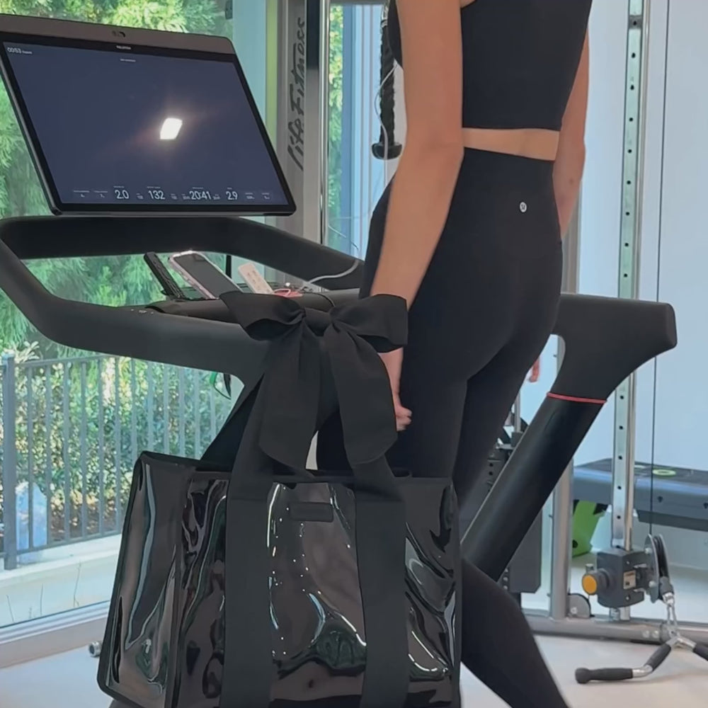 A woman working out in a home gym showing off her black jelly tote bag 