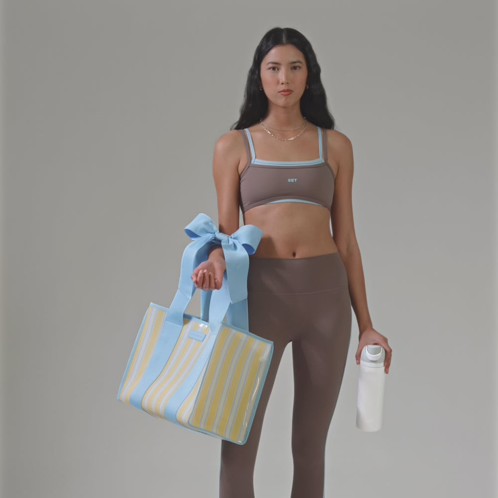 A woman in a brown workout outfit showing off her cabana stripe jelly tote
#color_cabana stripe bow