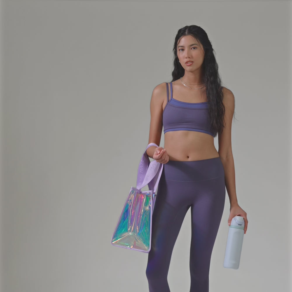 A woman showing how big the jelly tote bag is by a water bottle #color_iridescent