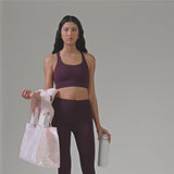 A woman in a plum workout outfit showing off her jelly tote bag and how big it is with. a water bottle
#color_ballet pink afternoon rosé bow