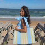 A woman showing off her Cabana Stripe Jelly tote bag on the beach 
#color_cabana stripe bow