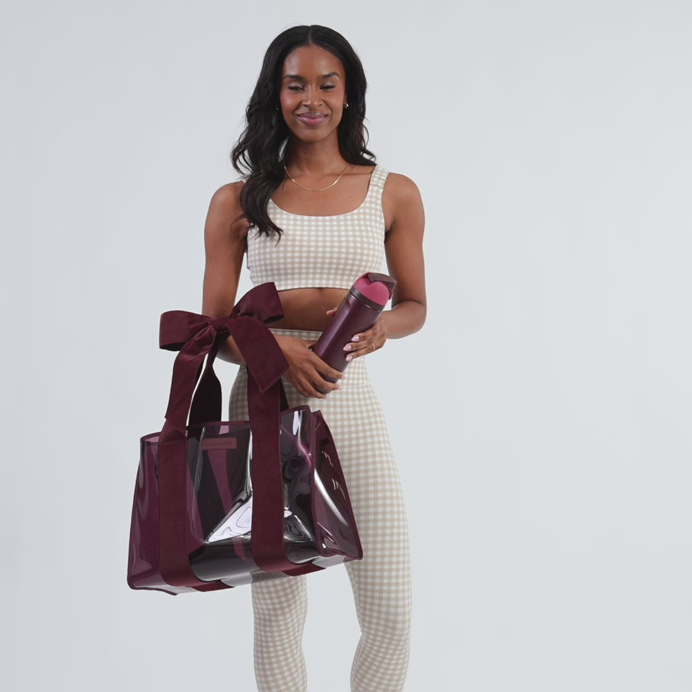 Woman walking into frame n a studio setting with the tote bag on her shoulder. She pauses to put a water bottle in her bag and then puts it back on her shoulder to walk off set.
#color_holiday edition red velvet bow