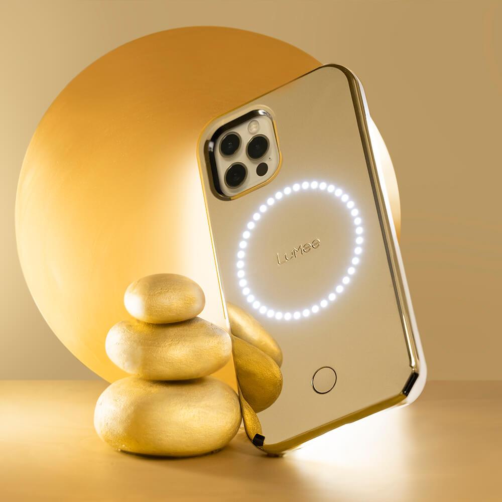 Gold mirror light up phone case propped up against a tower of gold rocks. color::Gold