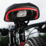 Grey AirTag sticker mount attached to underside of red and black bicycle seat cover.