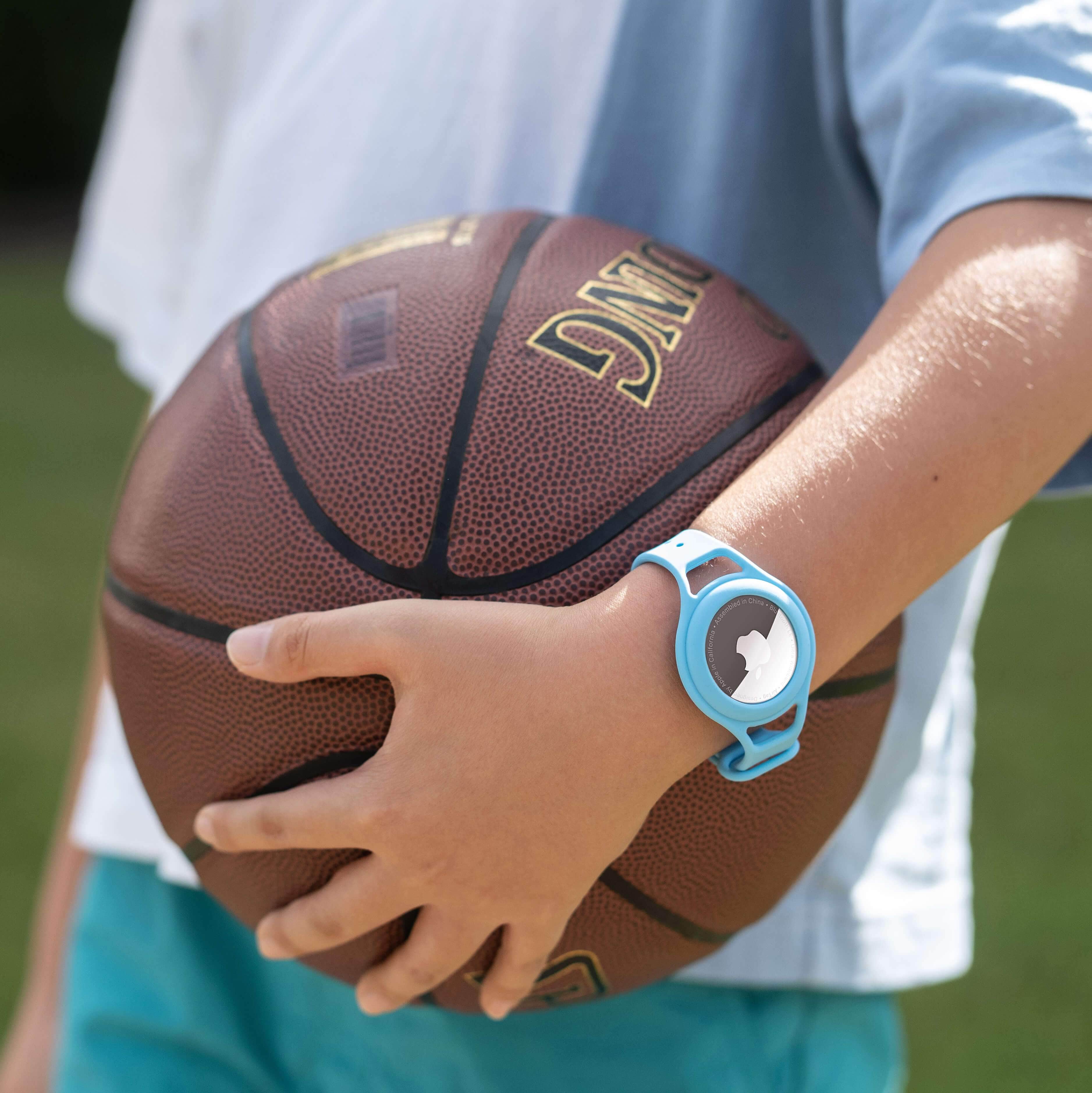 Kid wearing AirTag holder bracelet while holding a basketball. color::Blue
