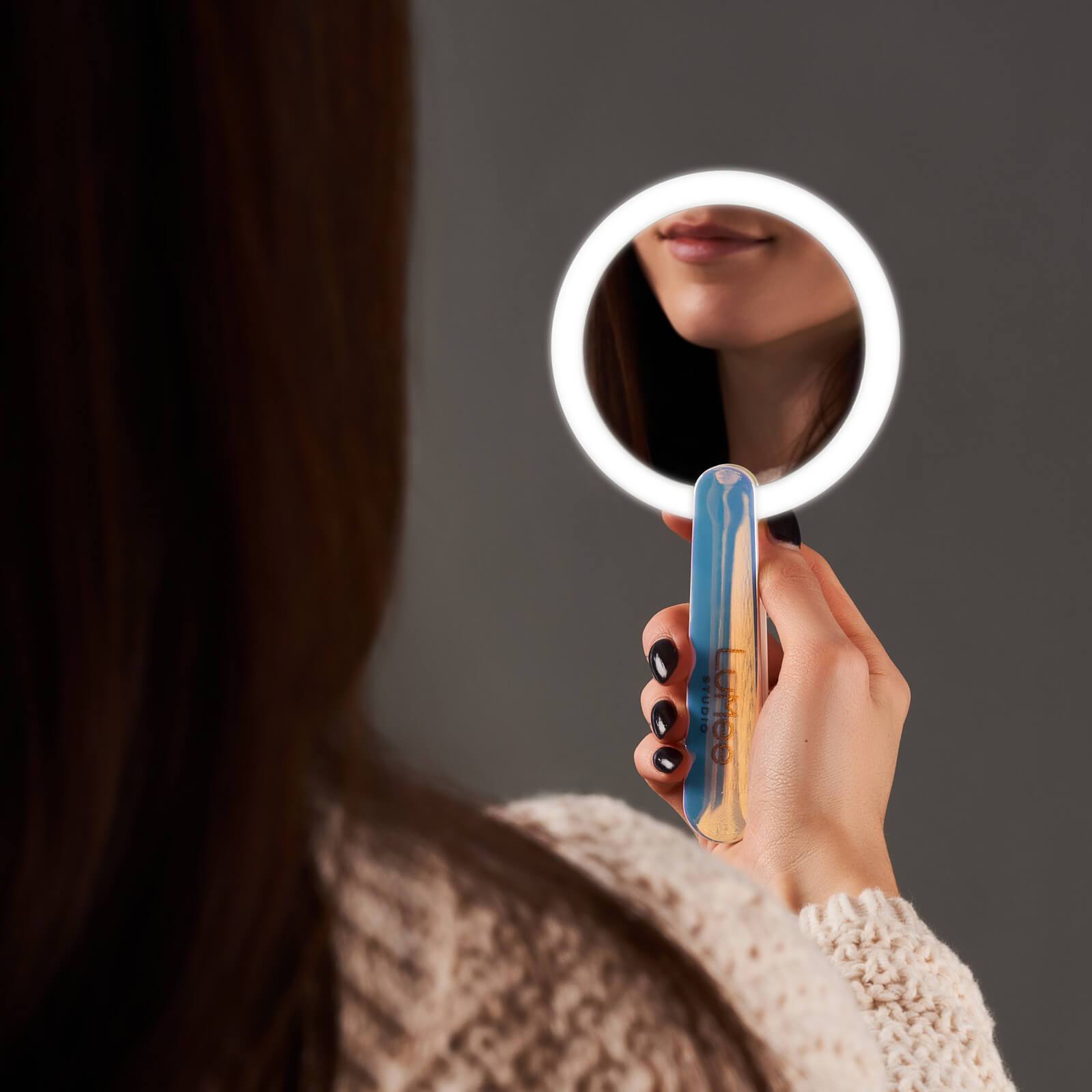 Hand holding light up handheld mirror with face reflecting. color::Iridescent