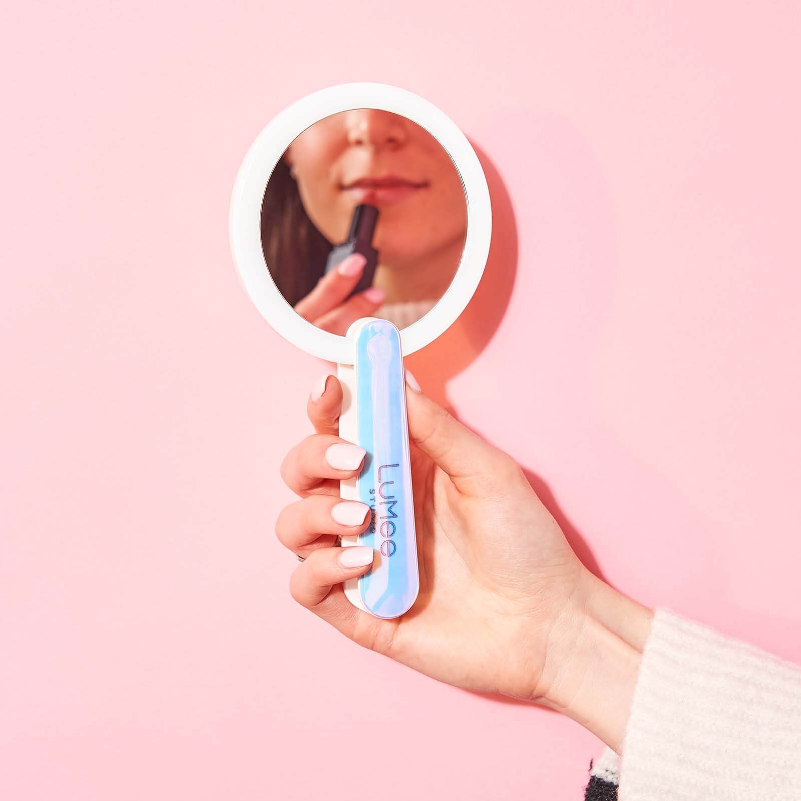 Woman applying lipstick in handheld light up mirror. color::Iridescent