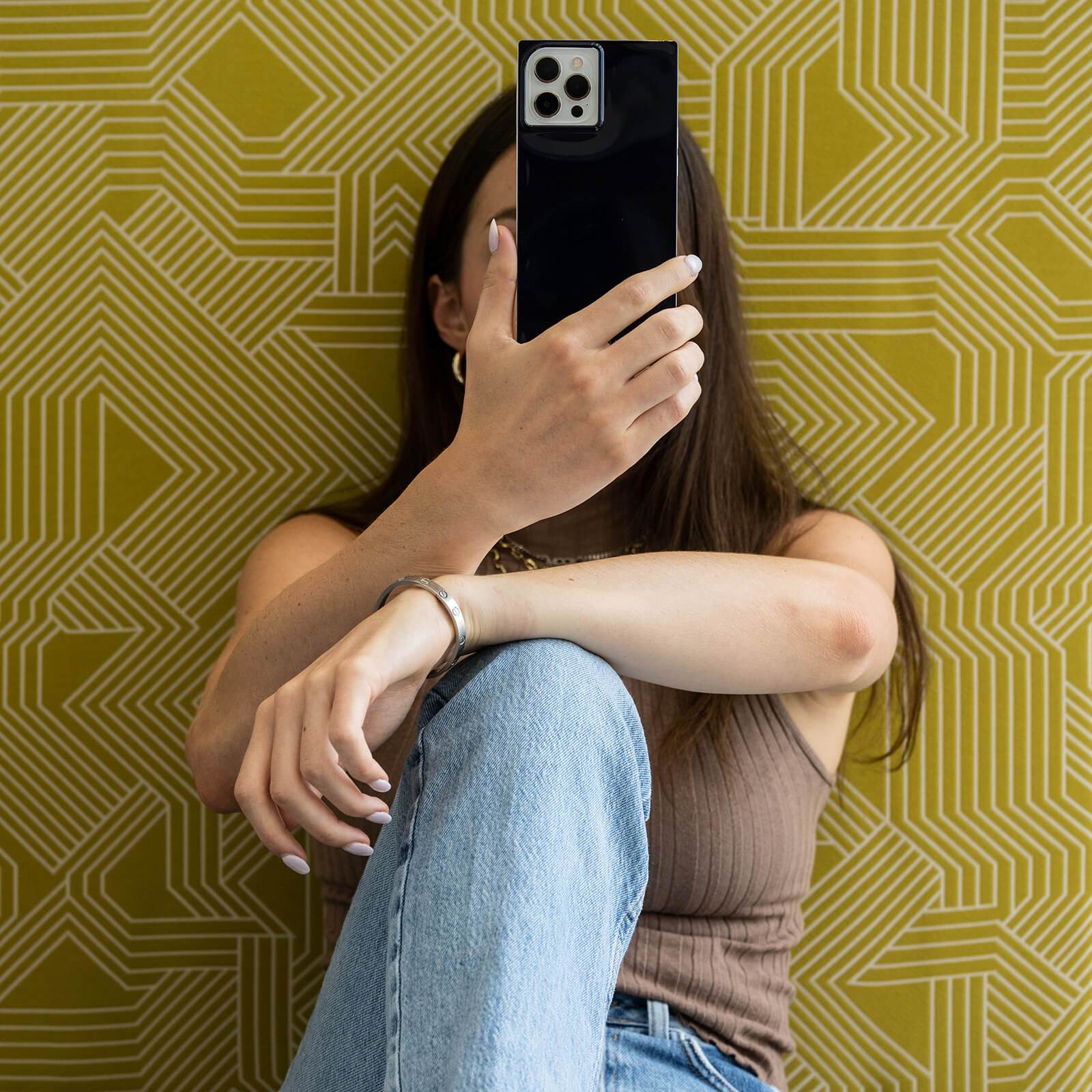 Woman holding black BLOX square case over her face. color::Black