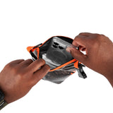 Hunter camo dry bag with orange trim being held open to display clear window viewing area inside.