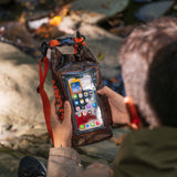 Hunter camo dry bag with red shoulder strap held in hand displaying smartphone inside clear window, near water.